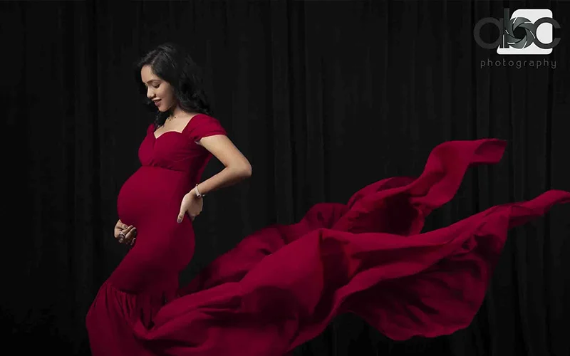 A pregnant woman elegantly dressed in a red maxi dress for her maternity photoshoot