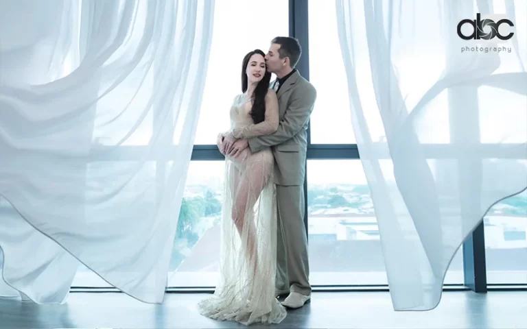 Couple embracing, sheer gown, light suit, flowing curtains, pregnancy photoshoot by abc photography