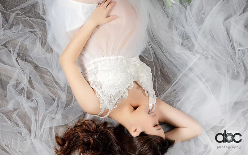 Pregnant woman lying on sheer fabric, maternity photoshoot by abc photography