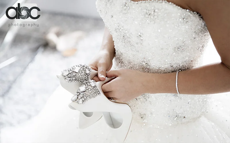 Bride holding embellished heels in beaded wedding gown