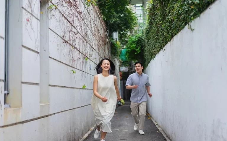 Couple wearing casual outdoor photoshoot outfits running through an alleyway.