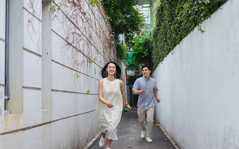 Couple wearing casual outdoor photoshoot outfits running through an alleyway.
