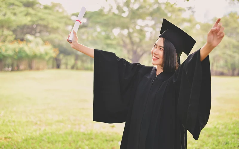 Graduate in academic gown posing for outdoor photoshoot in park.