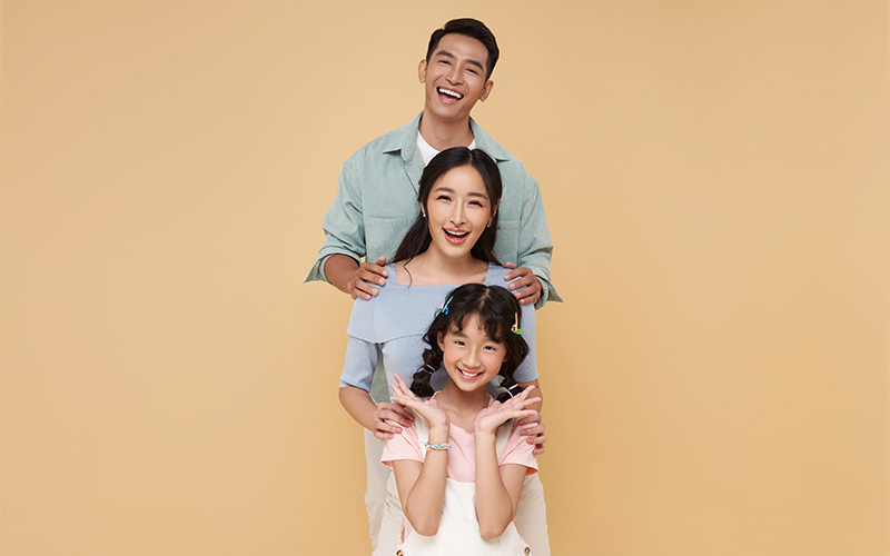 Three people posing together against beige background.