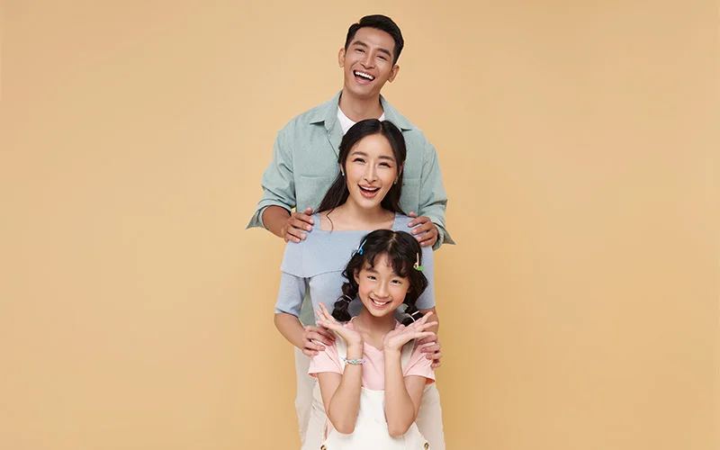 Three people posing together against beige background.