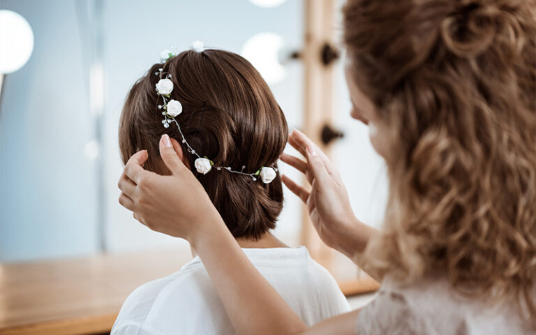 A hairstylist adding a delicate floral vine to a soft, tucked-under hairstyle