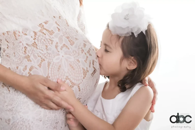 Girl kissing mother's baby bump