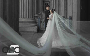 A dramatic black and white wedding portrait of a couple standing among grand classical columns