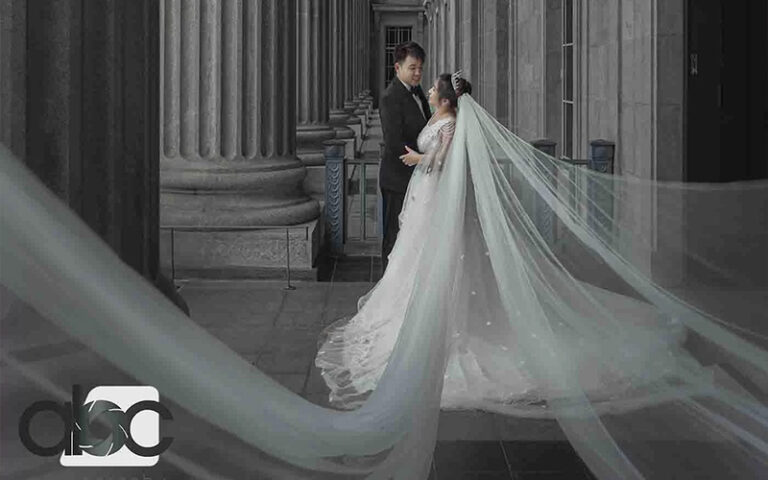 A dramatic black and white wedding portrait of a couple standing among grand classical columns