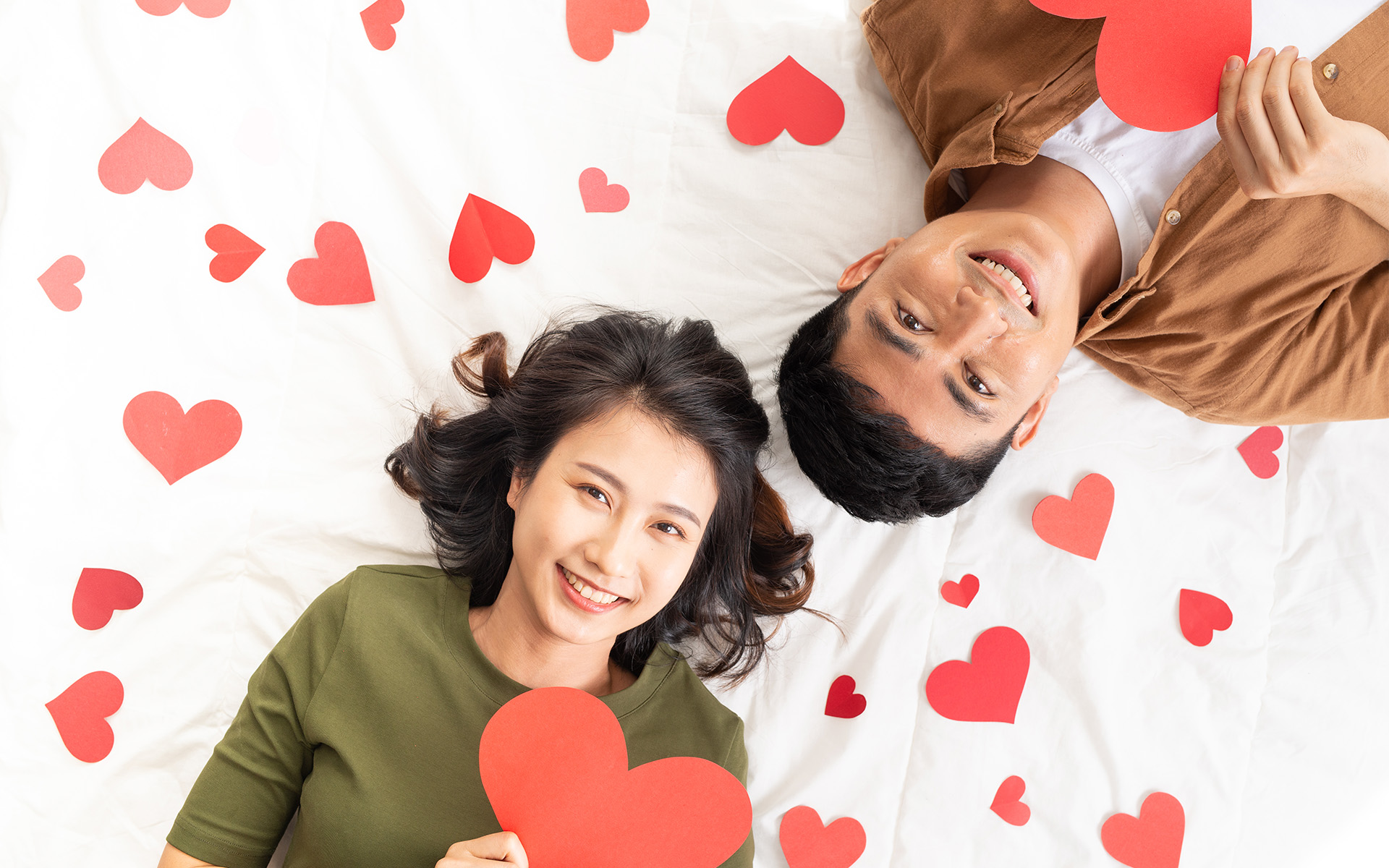 Smiling couple lying together with red paper heart props